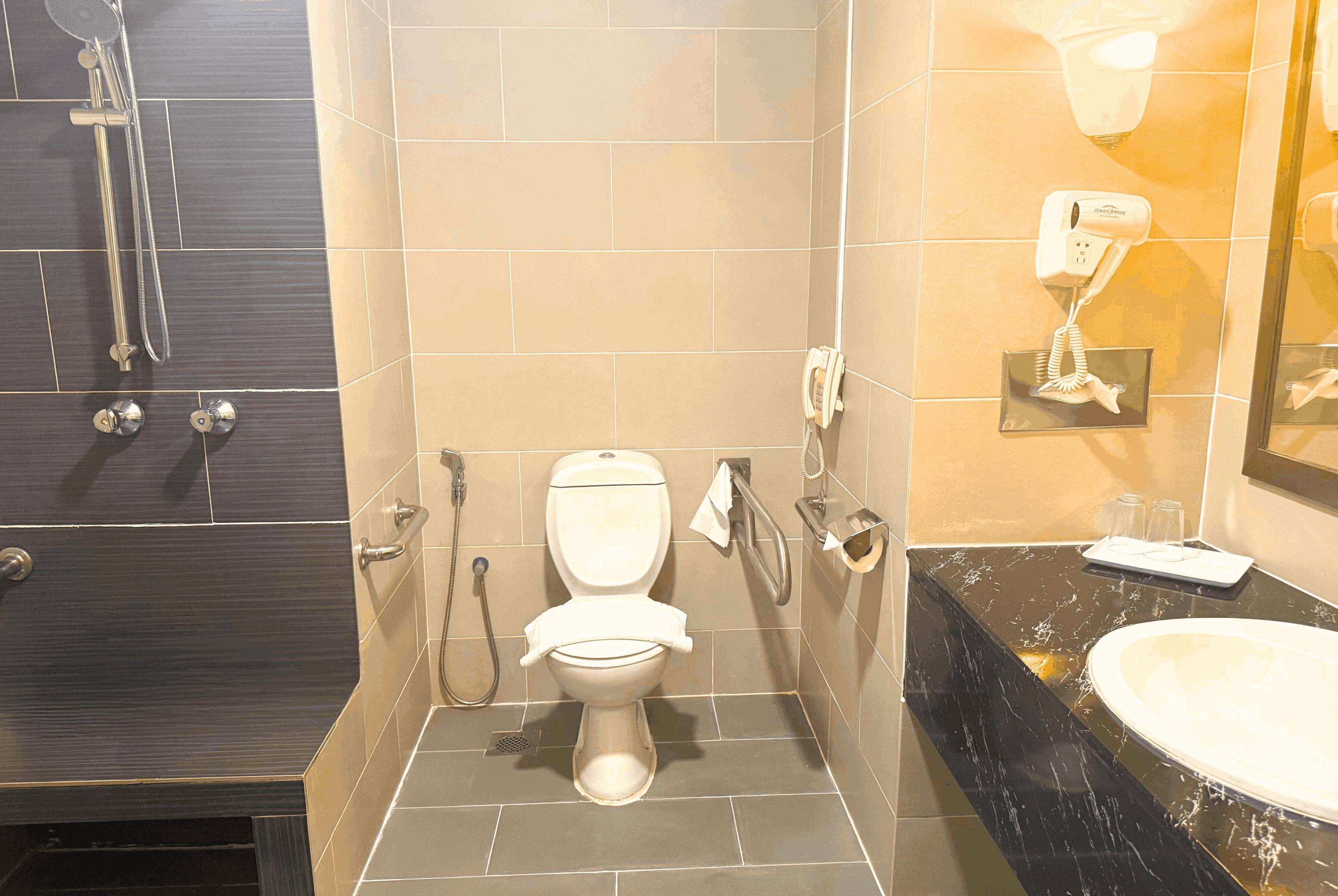 A bathroom with a toilet, a shower, a vanity with a sink, and a hairdryer mounted on the wall.
