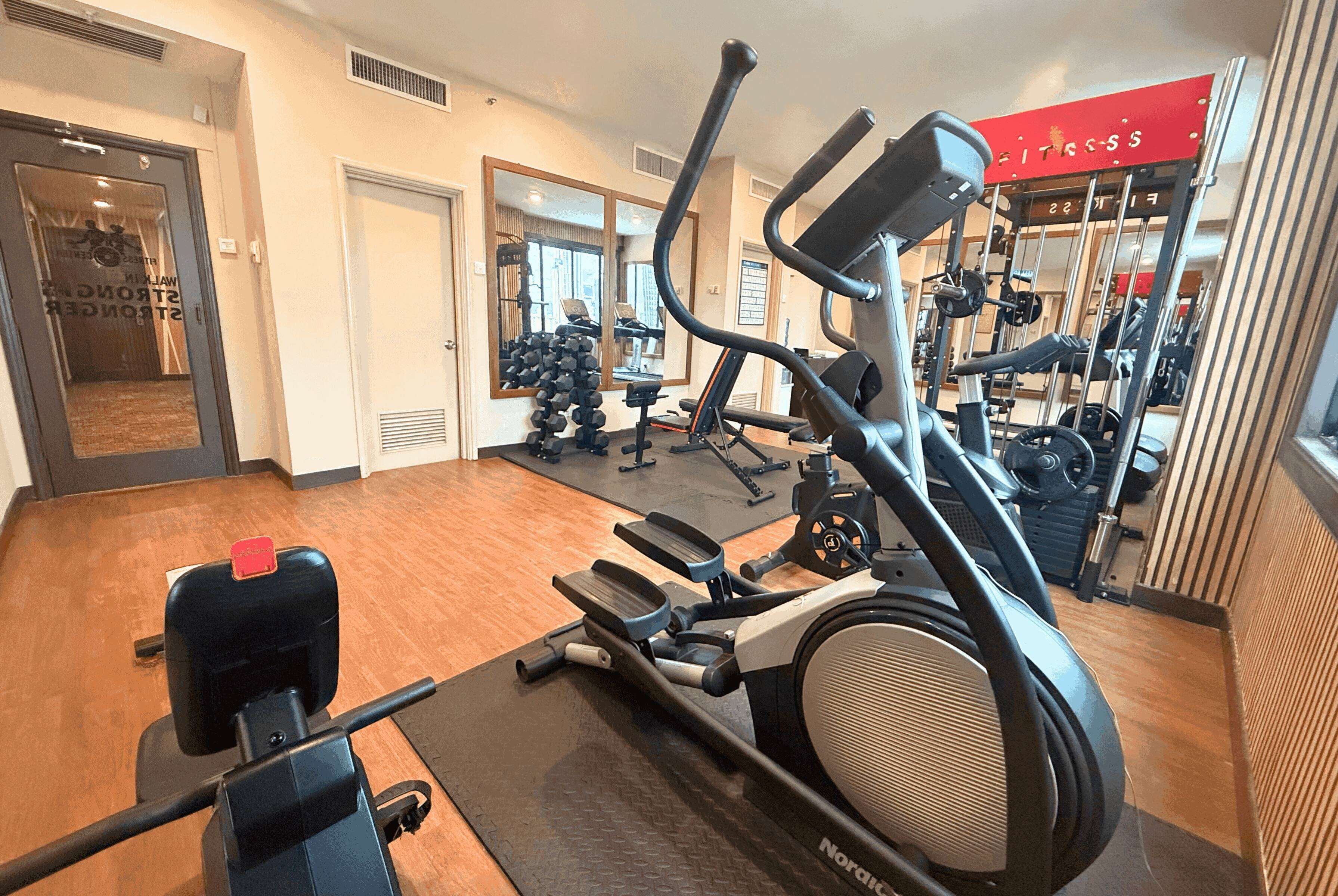 Un gimnasio con equipamiento de cardio, máquinas de pesas y un espejo grande.