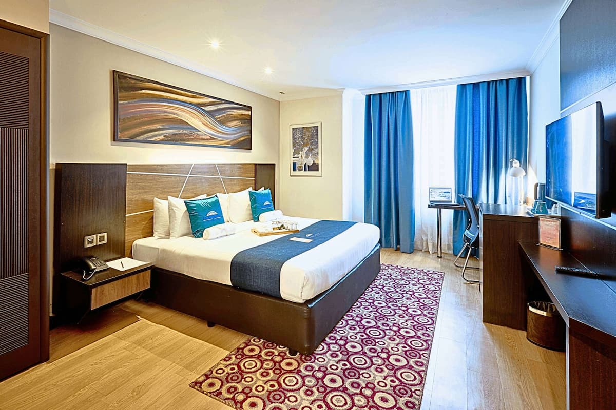 A hotel room with a large bed, a desk, a television, and a window with curtains.