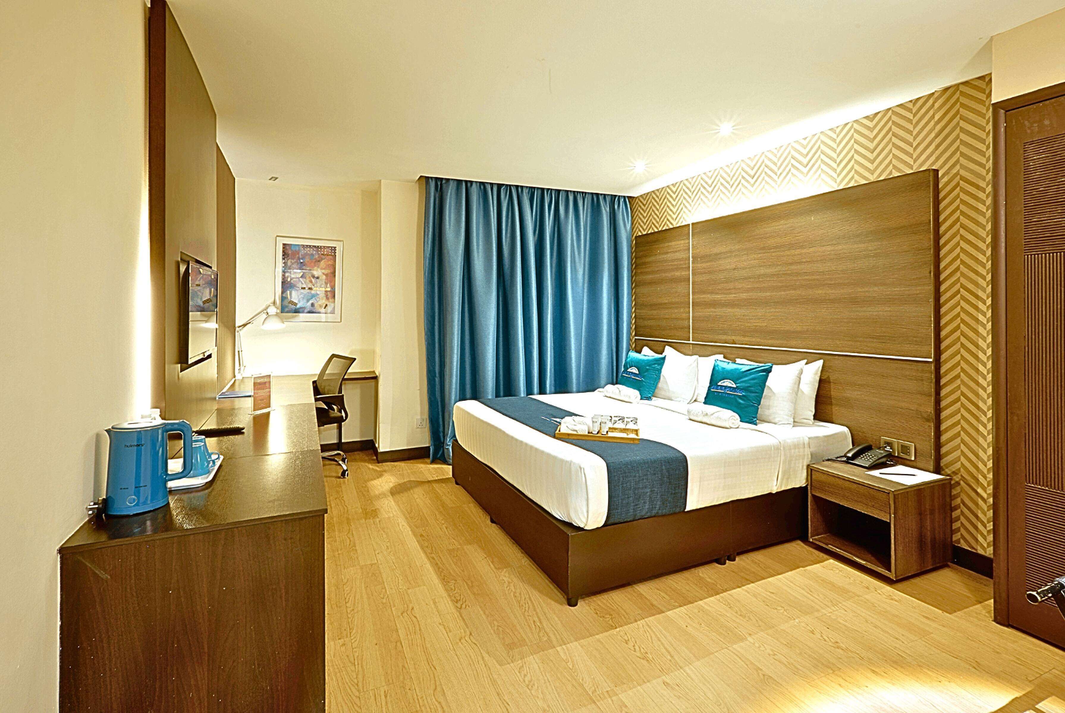 A hotel room with a large bed, a desk with a coffee maker, a nightstand, and a wooden headboard.