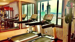 A gym with treadmills and exercise equipment, large windows with a city view, and a mirror reflecting the equipment. - Howard Johnson By Wyndham Kuala Lumpur 118 (Kuala Lumpur)