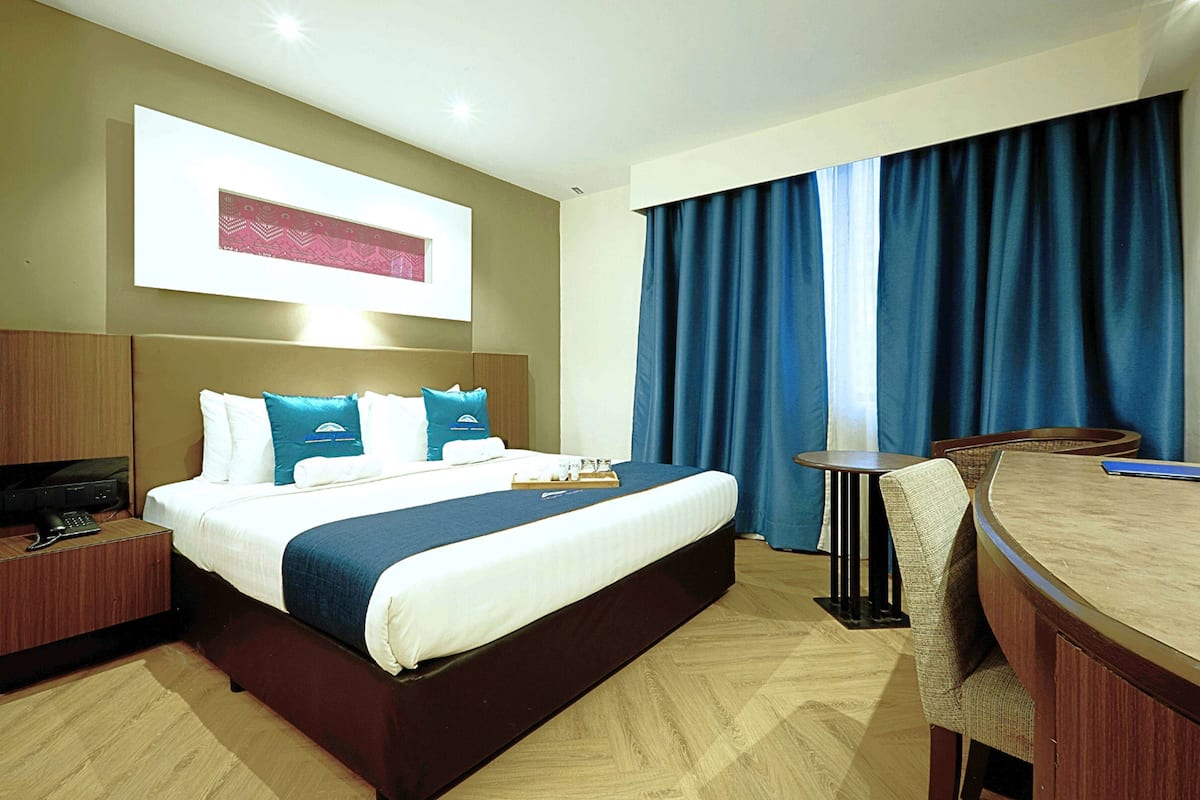 A hotel room with a large bed, a desk with a chair, a television, and a window with curtains.