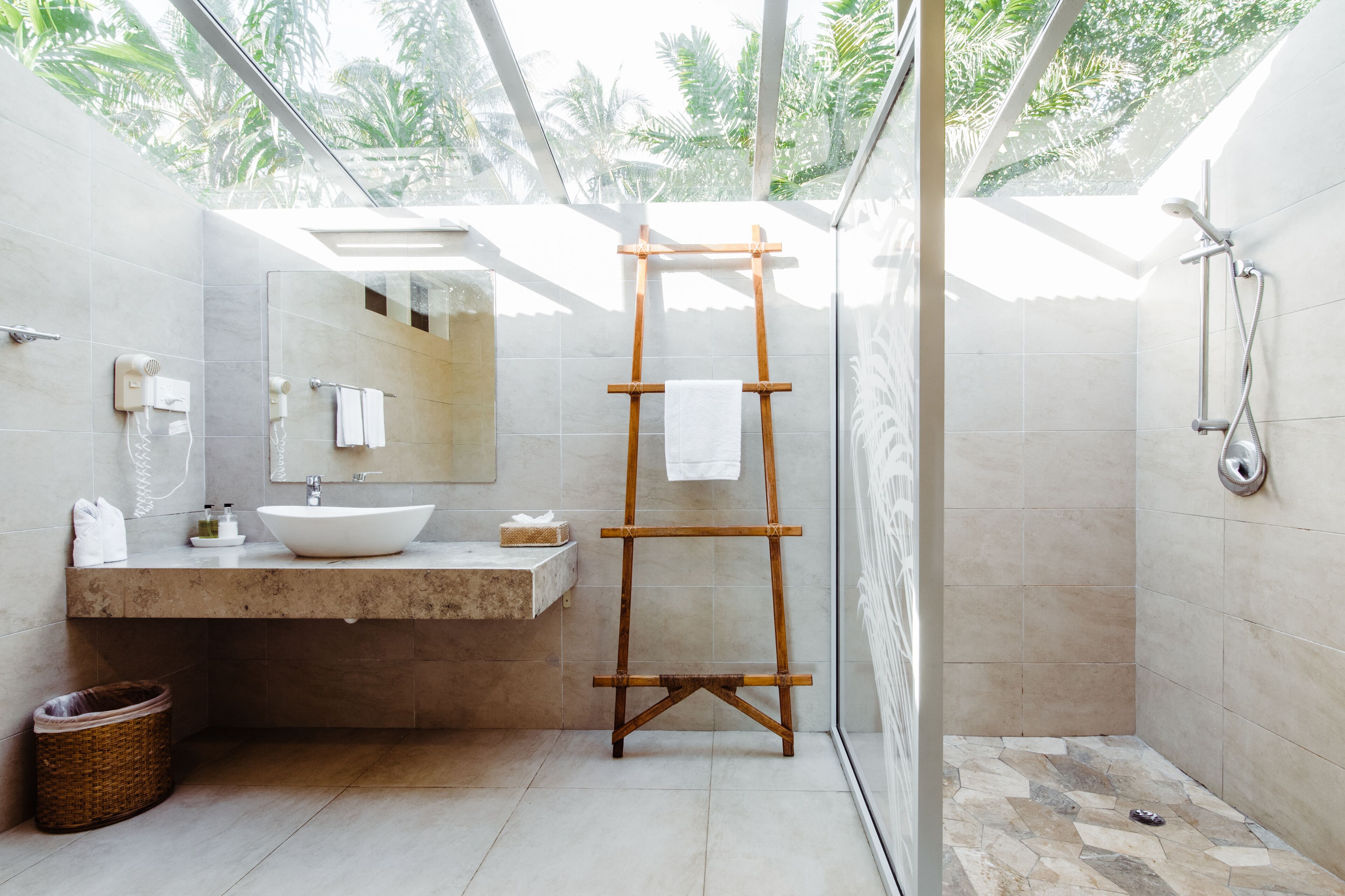 Un baño moderno con un espejo grande, un toallero de madera, un lavamanos y una zona de ducha.