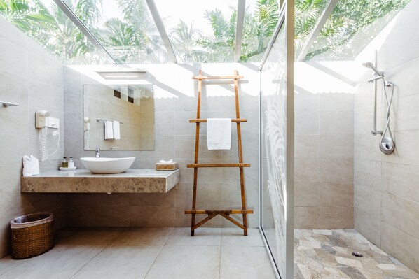 Un baño moderno con un espejo grande, un toallero de madera, un lavamanos y una zona de ducha.