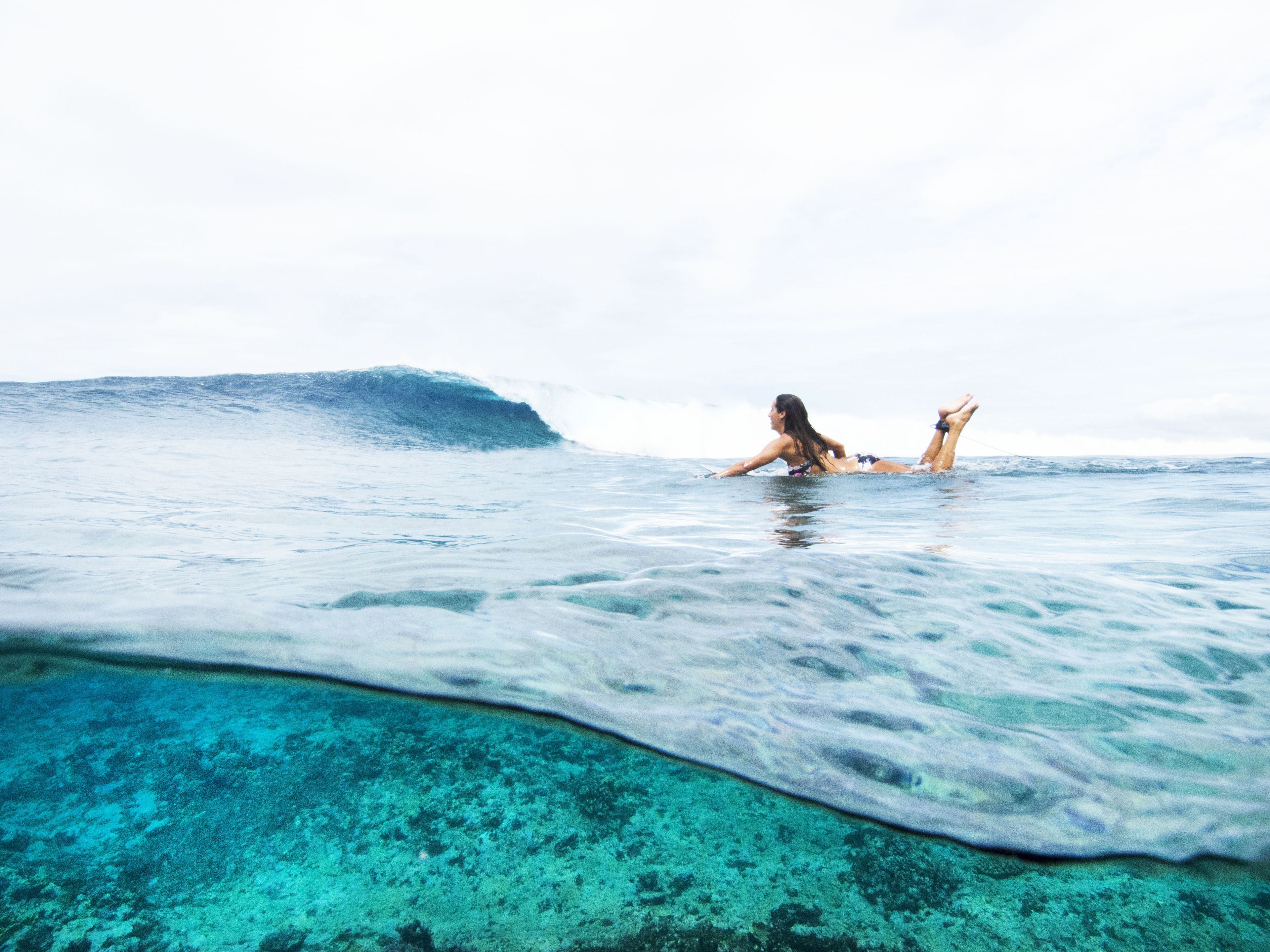 A person lying on a beach with a clear view of the ocean and a wave in the background.