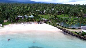 A beach resort with a sandy beach, clear turquoise water, and numerous palm trees. There are several lounge chairs and umbrellas on the beach, and a few people swimming in the water. - Sinalei Reef Resort & Spa (Siumu)