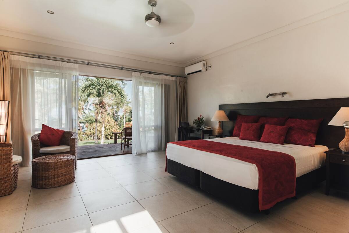 Un dormitorio amplio con una cama grande, una silla, una mesita y vistas al exterior.