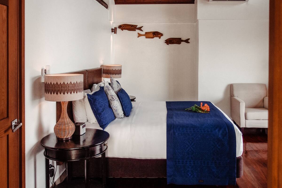 Una habitación de hotel con una cama, una mesita de noche con lámpara, una silla y peces decorativos en la pared.