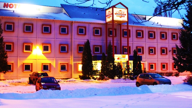 A hotel with a snow-covered parking lot and multiple cars parked in front.