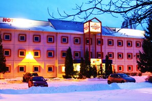 A hotel with a snow-covered parking lot and multiple cars parked in front.