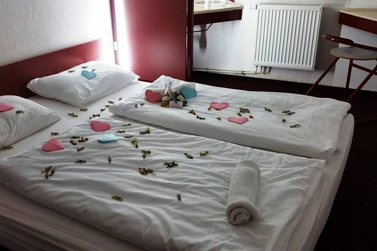A hotel room with two beds, each with white linens, heart-shaped pillows, and small decorative items.