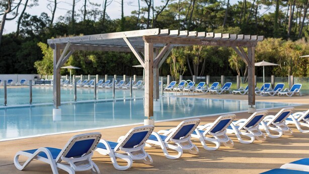 Un área junto a la piscina con sillas de descanso y una pérgola.