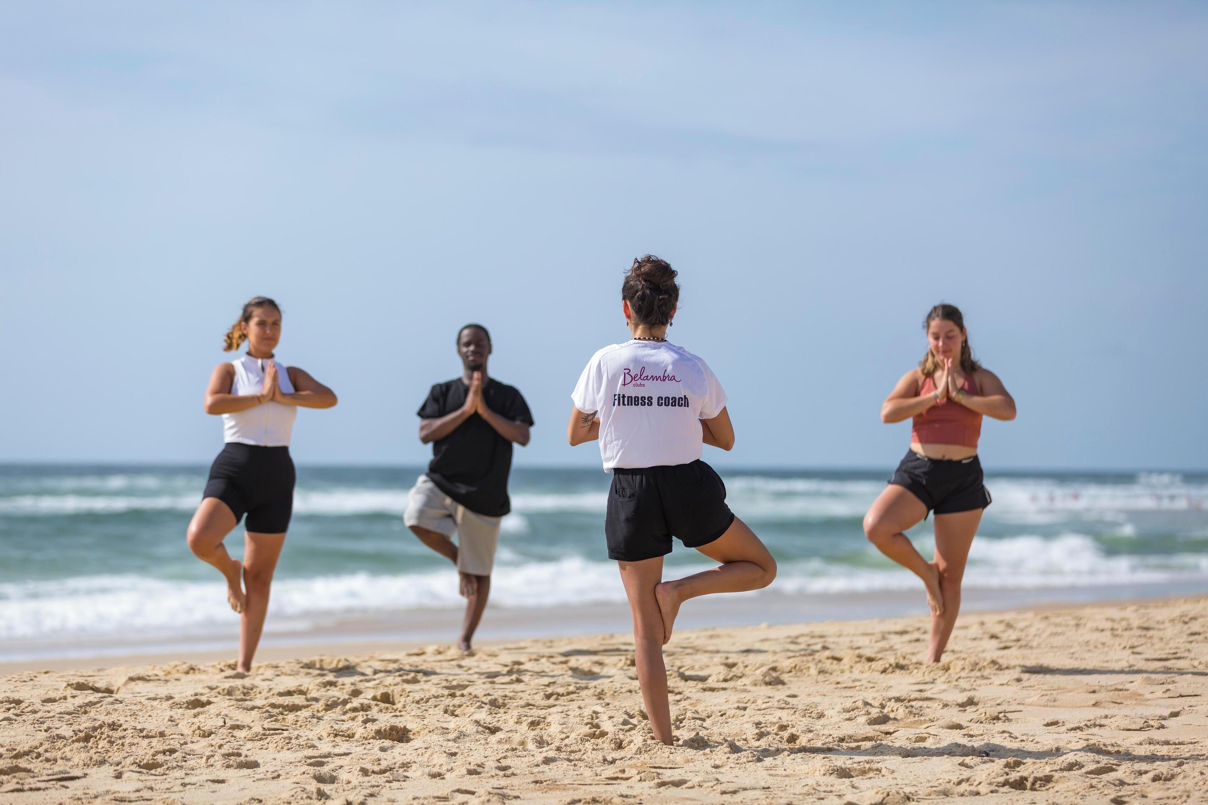 Un groupe de personnes pratiquant une posture de yoga sur une plage, avec l’océan en arrière-plan.