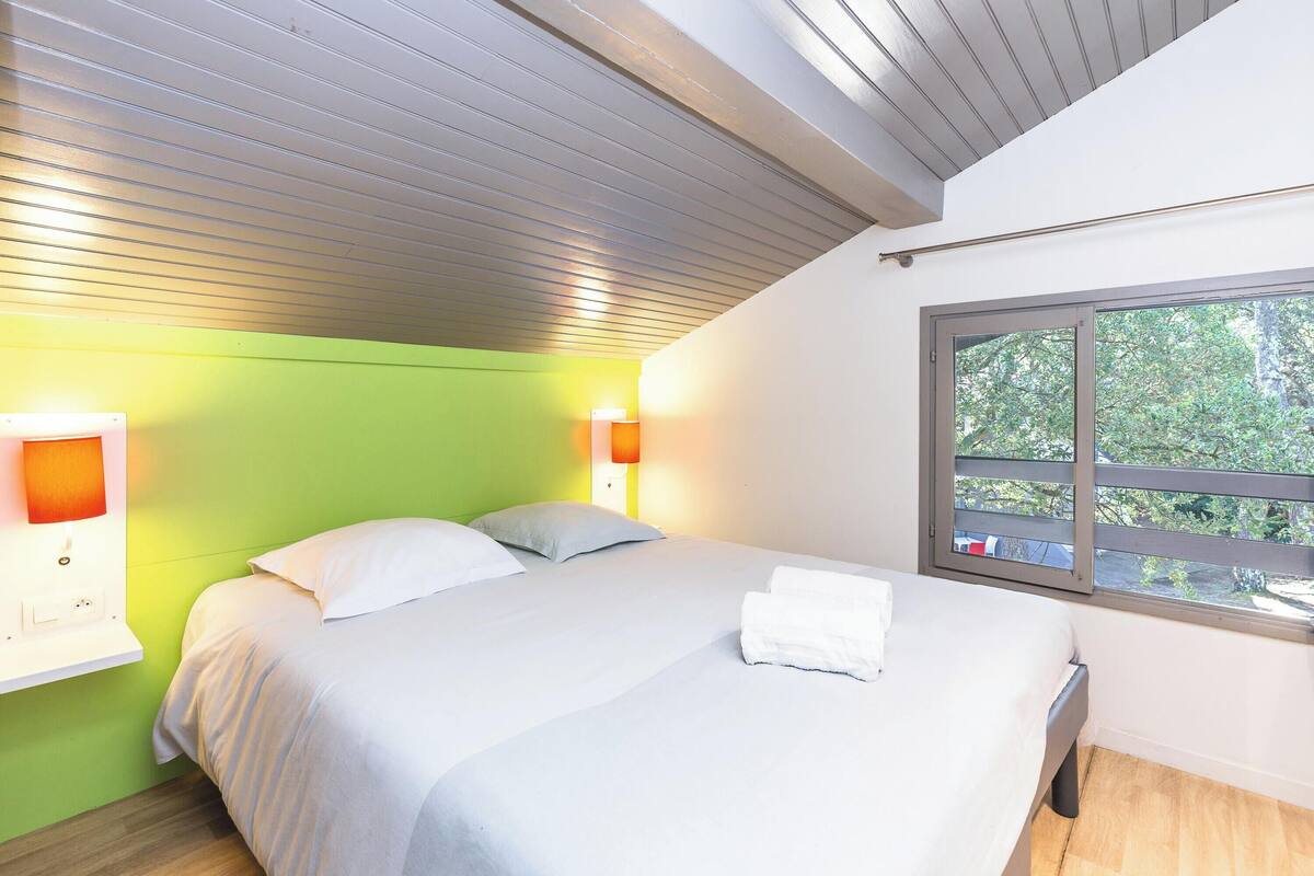 Un dormitorio con una cama, dos lámparas de pared, un ventanal con vistas y una pared verde.