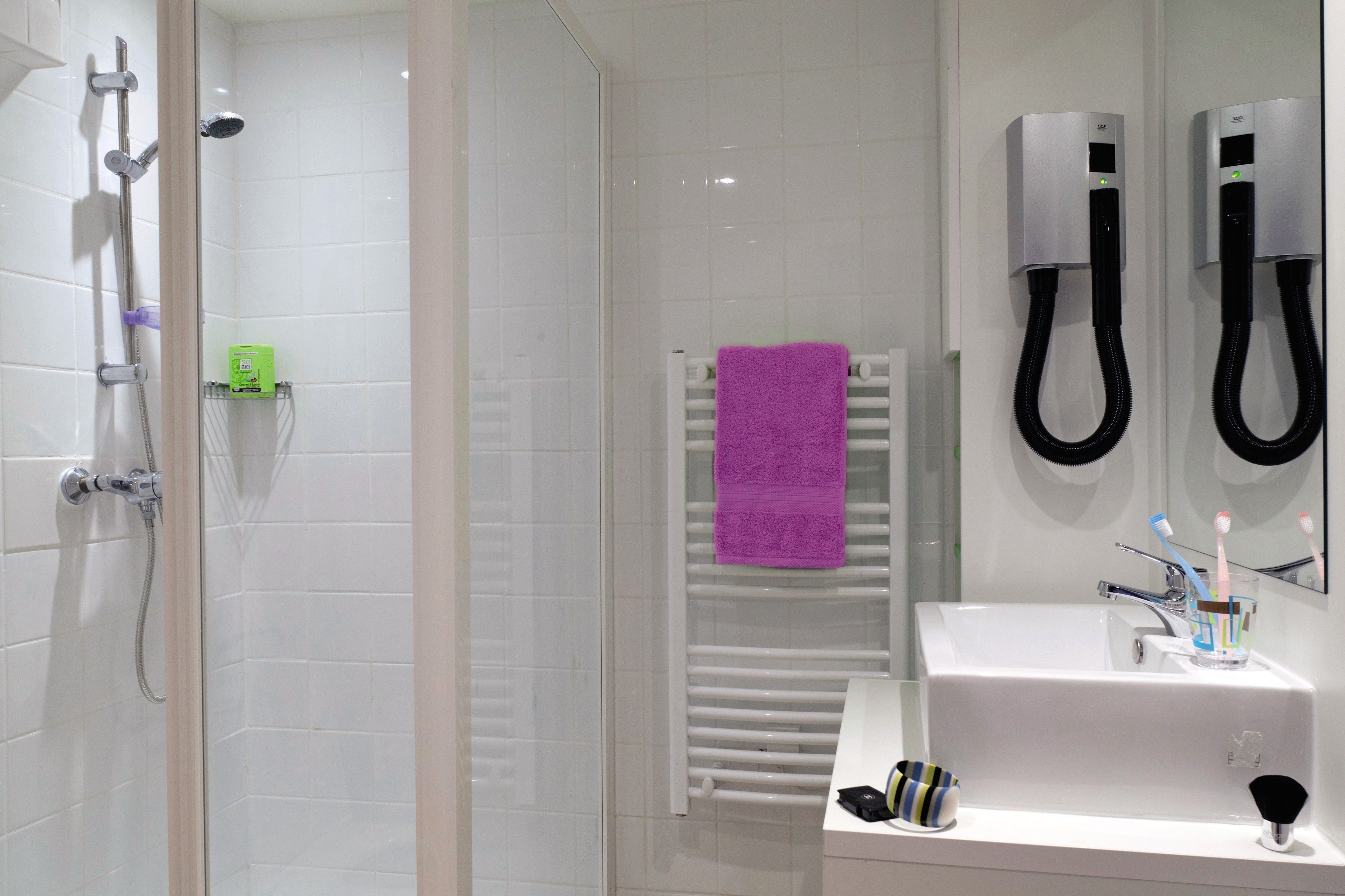 Une salle de bain moderne avec une douche à parois de verre, un lavabo blanc avec un miroir et un porte-serviettes sur lequel est posée une serviette violette.