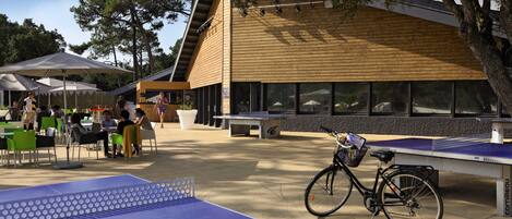 An outdoor seating area with tables and chairs, a ping pong table, and a bicycle parked by a bench.