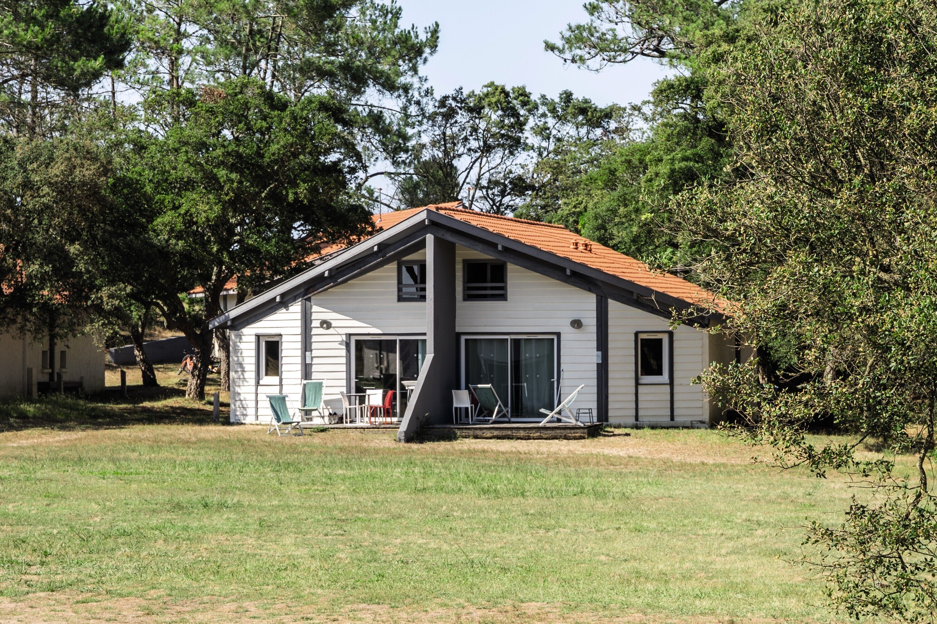 Une maison de plain-pied avec un toit en tuiles, une terrasse couverte et une pelouse devant.
