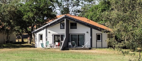 Une maison de plain-pied avec un toit en tuiles, une terrasse couverte et une pelouse devant.