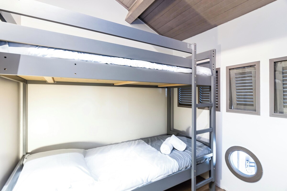 Una cama litera con cabecera, una ventana con persianas y un ventanal circular.