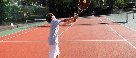 A tennis court with a net, a player in a white shirt and shorts, and a tennis ball in motion.