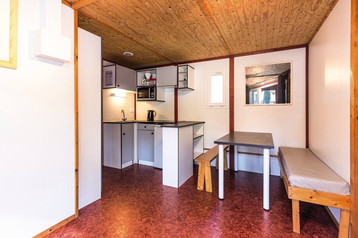 Una cocina compacta equipada con microondas, cafetera y lavabo. Cuenta con una pequeña mesa de comedor y un banco.