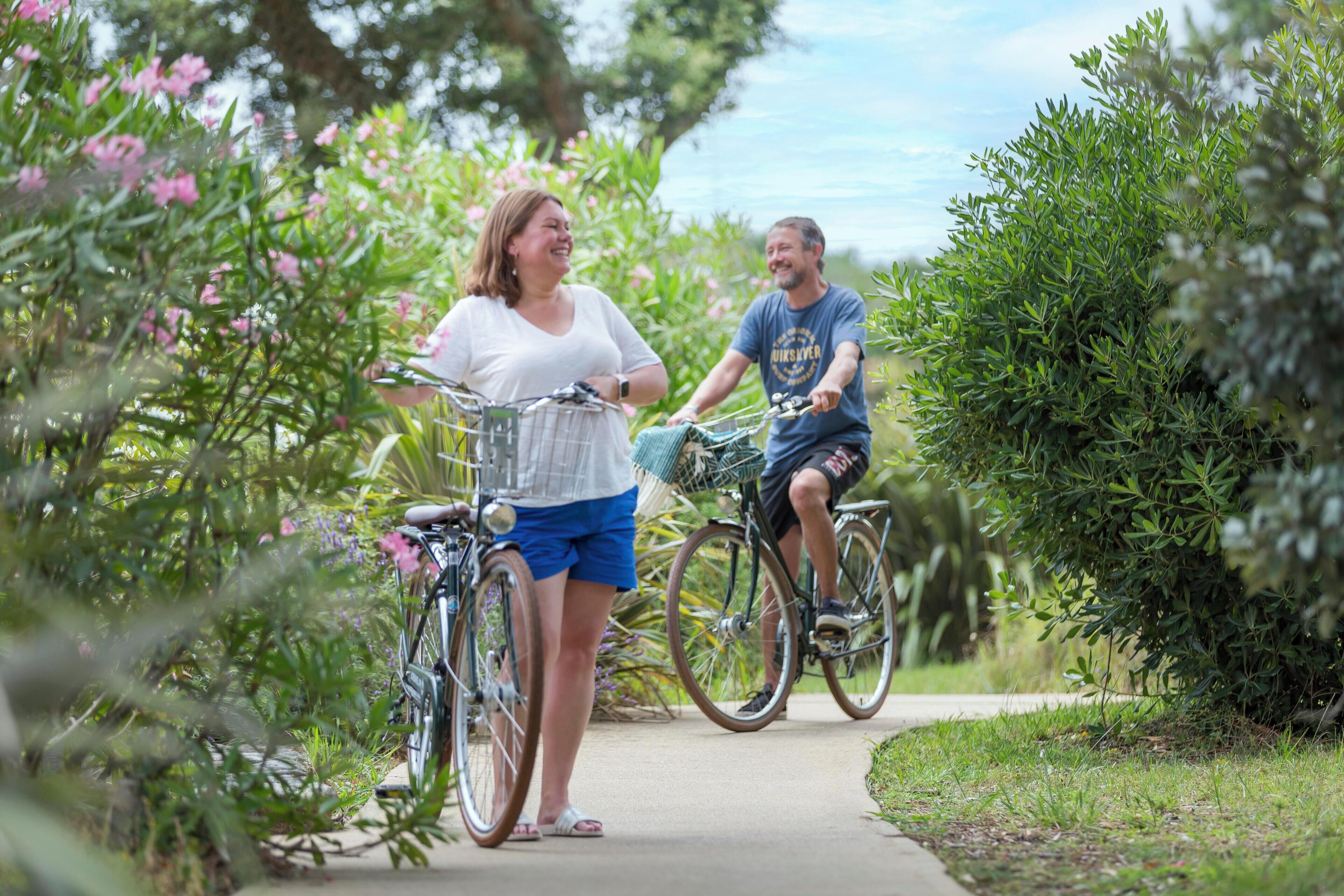 Two people on bicycles in a garden path surrounded by greenery.