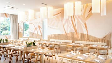 Interior de un restaurante moderno con mobiliario de madera, iluminación colgante y vistas al exterior con vegetación.