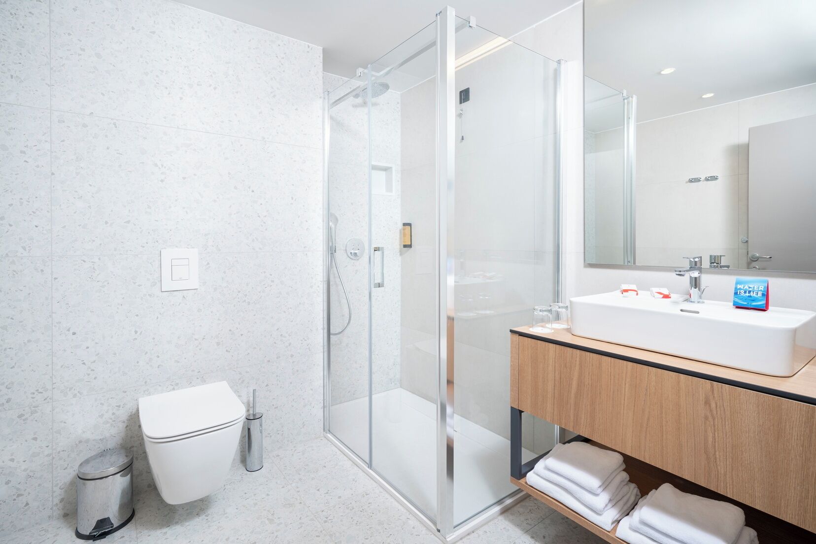 A modern bathroom with a glass-enclosed shower, a white sink, and a mirror above it.