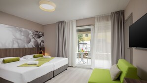 Hotelkamer met een bed, een groene bank, een televisie en een balkon met een tafel en stoelen.