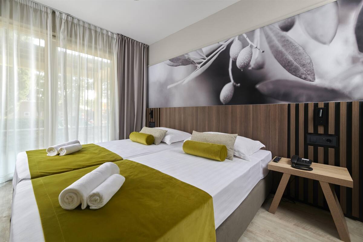 Ein Hotelzimmer mit einem großen Bett, zwei Kissen, einem Nachttisch mit Telefon und Lampe sowie einem an der Wand montierten Fernseher.