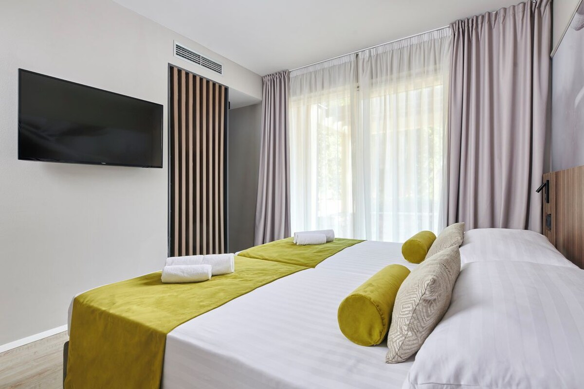 Une chambre d’hôtel avec un lit, une télévision, une fenêtre avec des rideaux et une bouche d’aération fixée au mur.