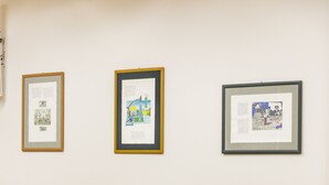 Een vergaderzaal met rijen stoelen en drie ingelijste kunstwerken aan de muur.