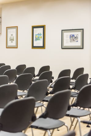 Une salle de conférence avec des rangées de chaises et trois œuvres d’art encadrées accrochées au mur.