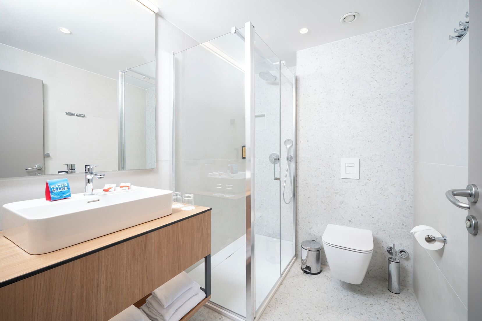 A modern bathroom with a glass-enclosed shower, a white sink with a mirror, and a toilet.