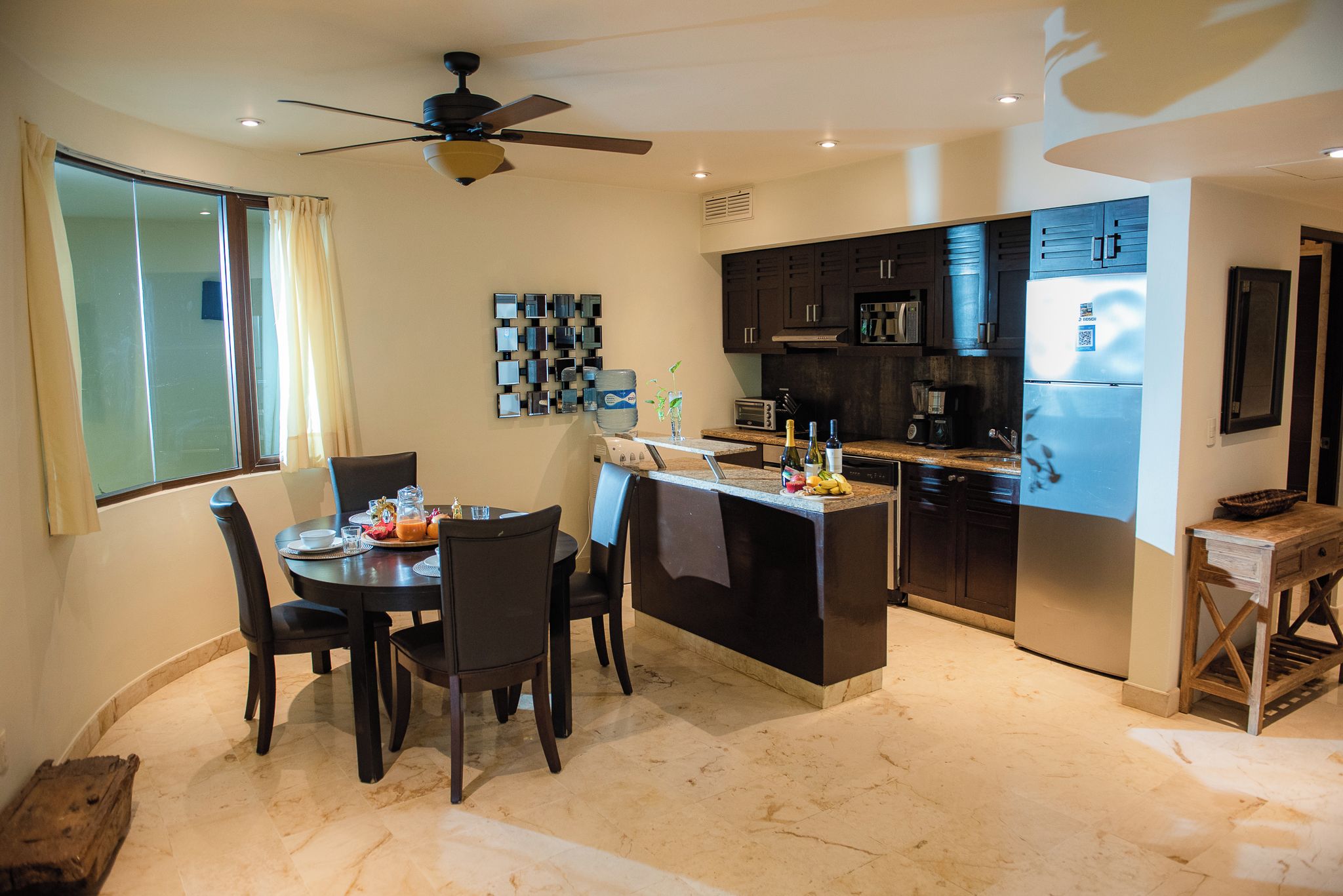 Una cocina moderna con armarios oscuros, una isla central y un comedor con una mesa redonda y sillas.