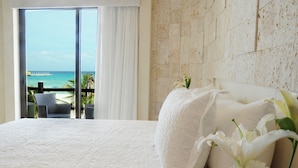Ein Hotelzimmer mit einem großen Bett, weißen Leinen, Meerblick und einem Balkon mit einem Sessel.