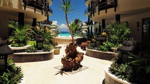 Ein Innenhof eines Resorts mit einer Palme, Topfpflanzen und Blick auf den Strand.