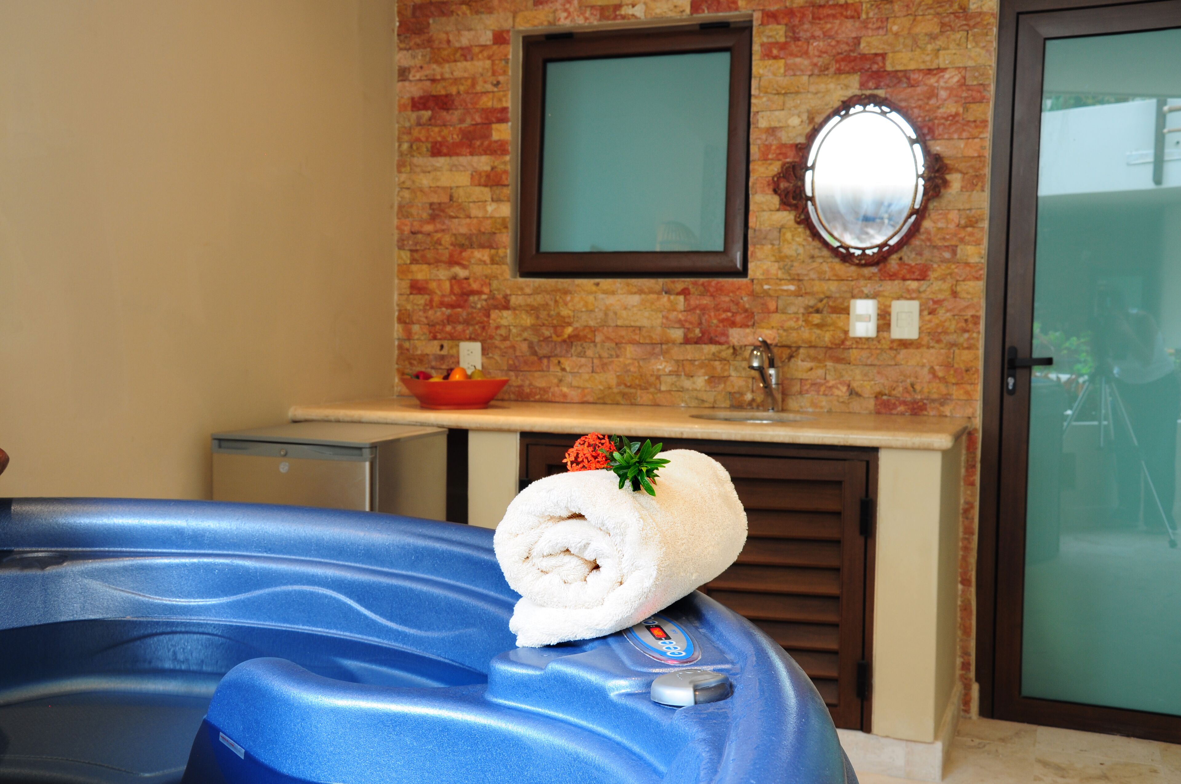 A bathroom with a brick wall, a mirror, a towel on a blue bathtub, and a small sink with a bowl of fruit.