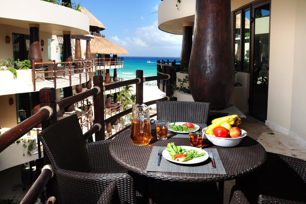 A dining area with wicker furniture, a table set with a pitcher of tea, plates of food, and a view of the ocean.