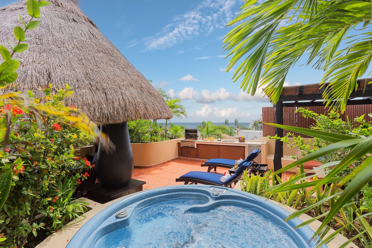 A hot tub with lounge chairs, a thatched roof structure, and a view of the ocean.