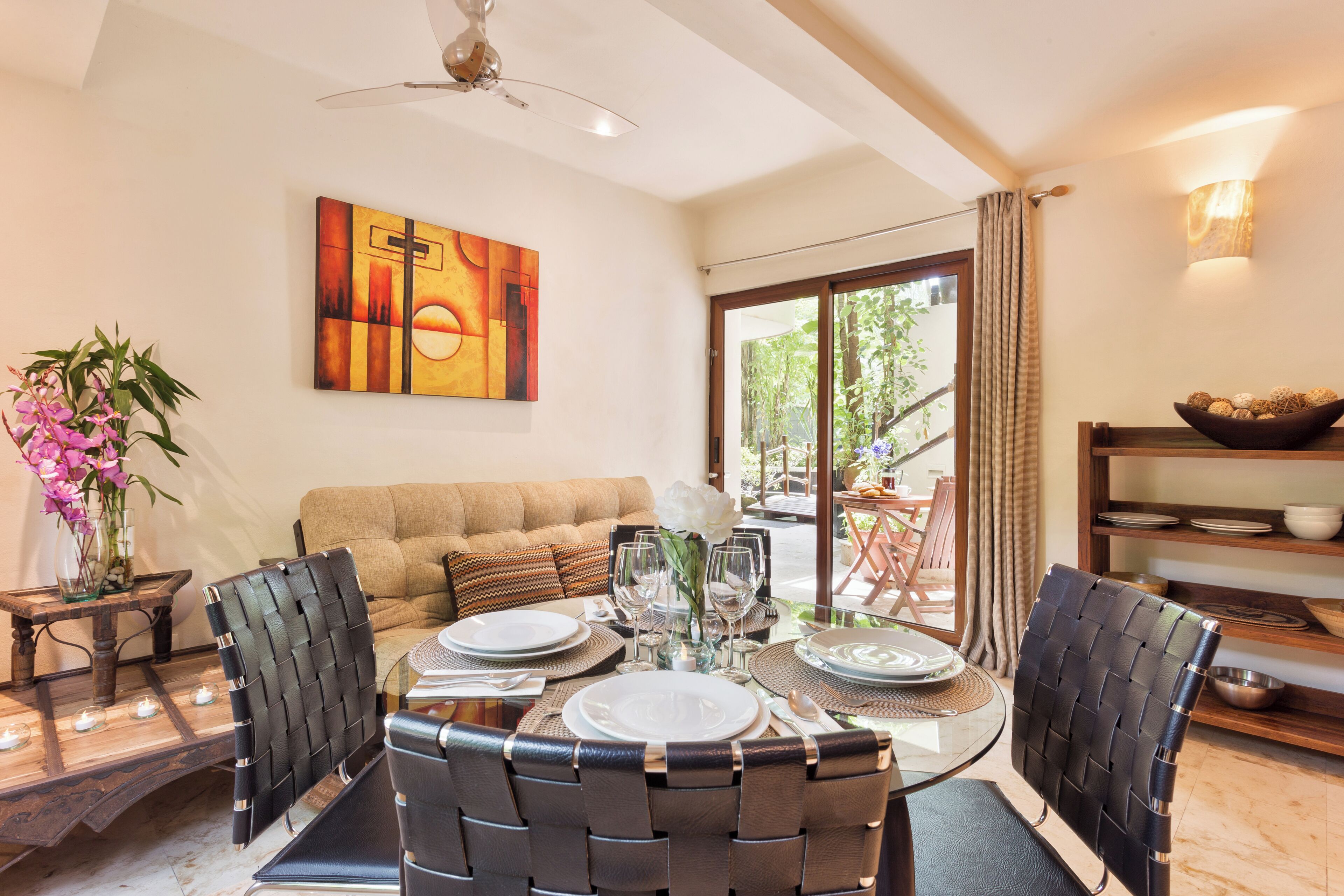 A dining area with a round table set for four, surrounded by black woven chairs. A large abstract painting is on the wall above the table.