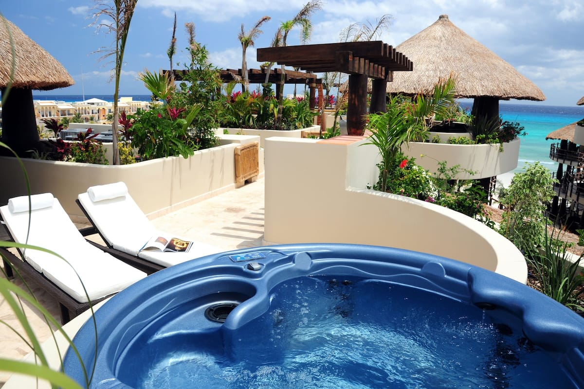 A hot tub surrounded by lounge chairs and a poolside area with a view of the ocean.