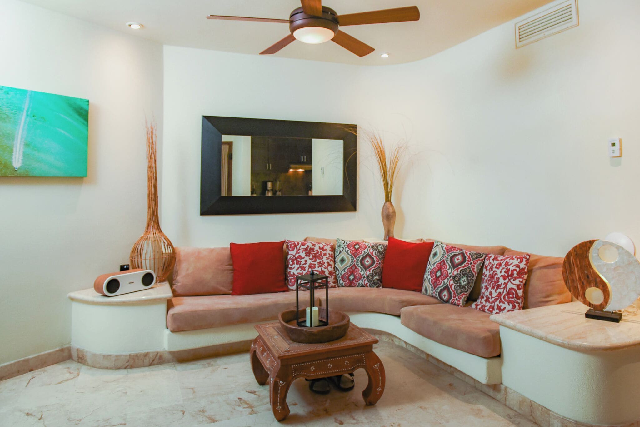 A living room with a sofa, a coffee table, a side table, a ceiling fan, a wall-mounted mirror, and a painting.