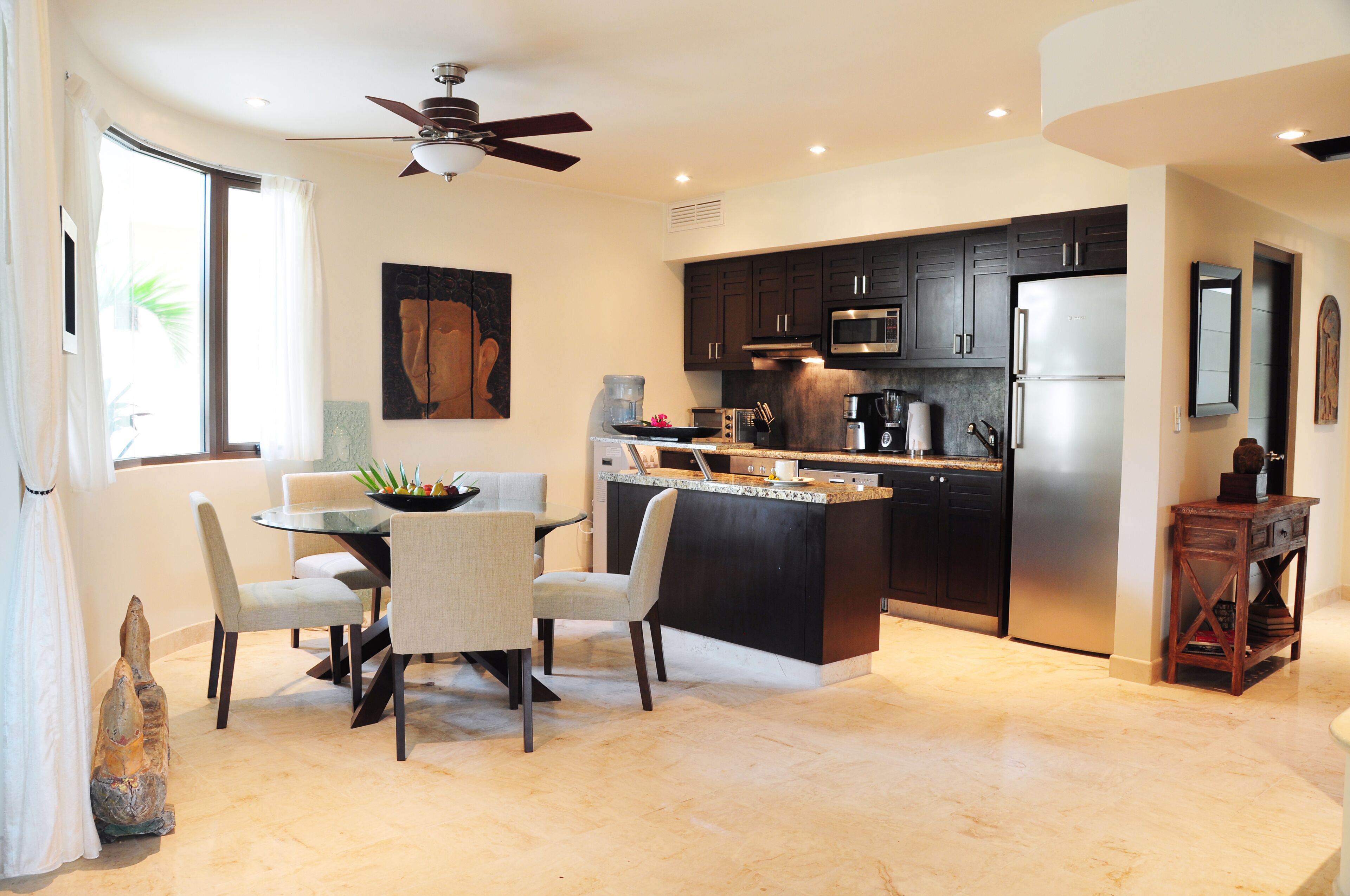 A modern kitchen with dark cabinets, a stainless steel refrigerator, and a dining area with a round table and chairs.