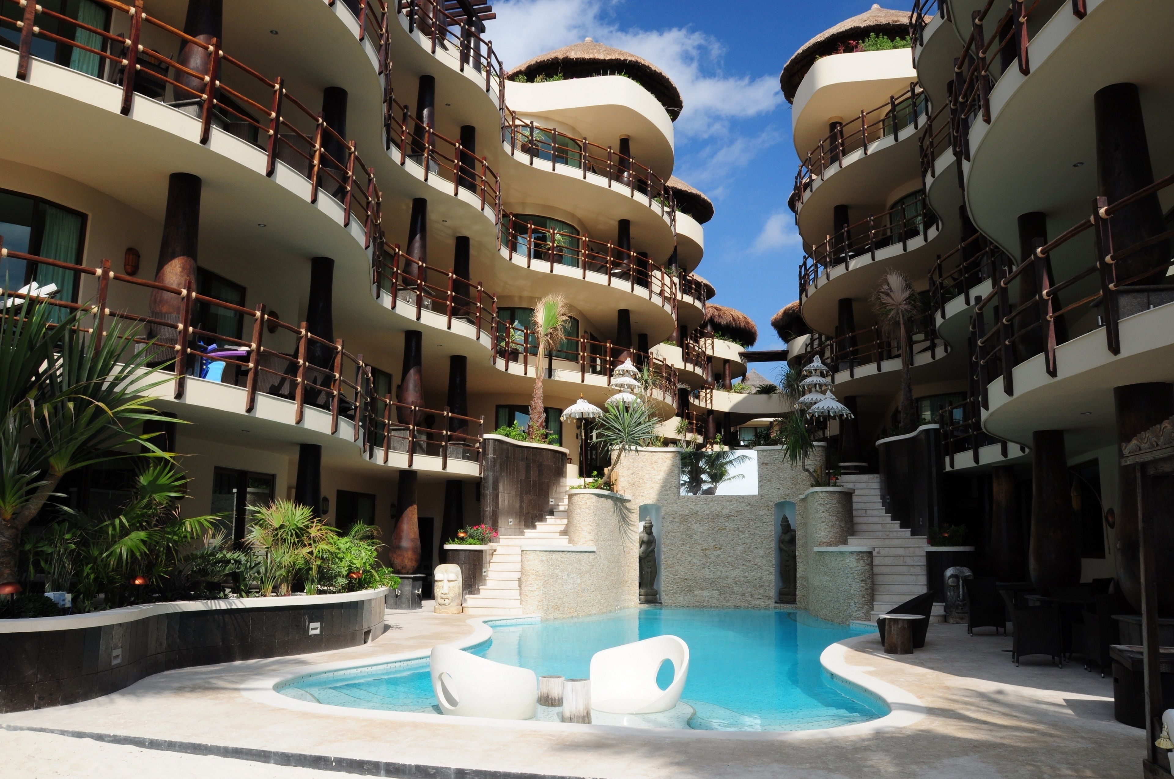 A multi-story hotel with a central pool, balconies, and tropical landscaping.