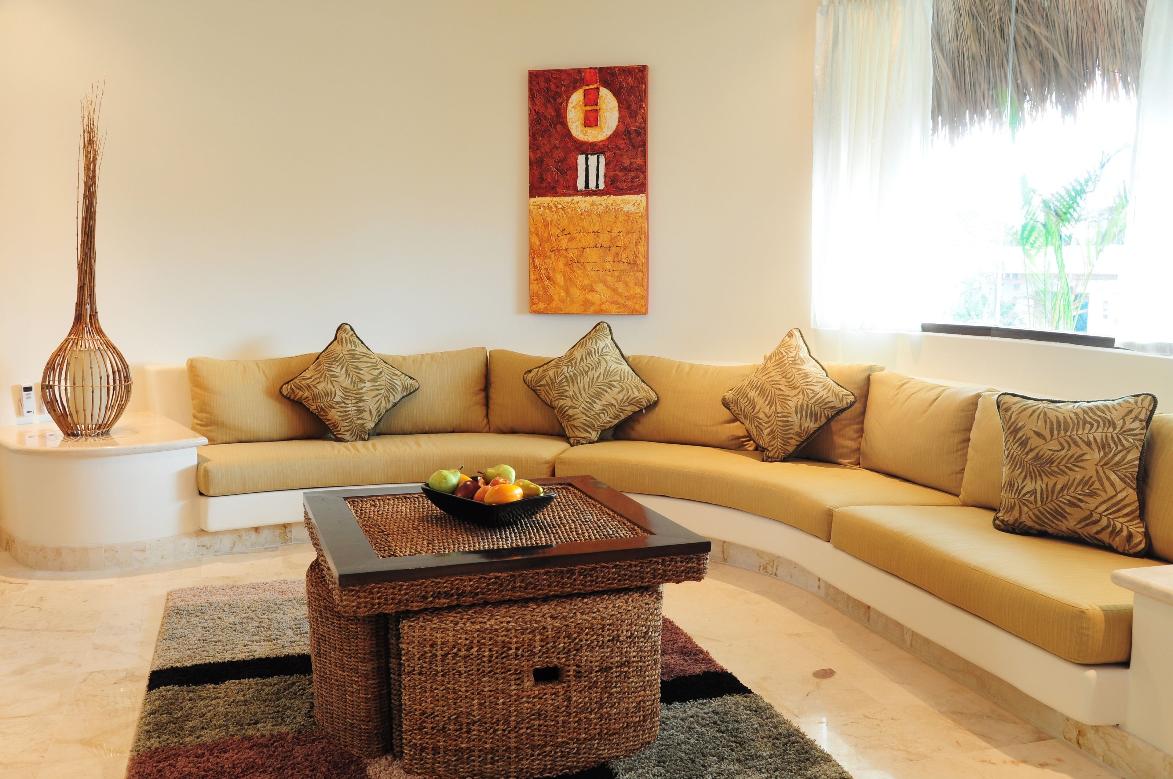 A living room with a beige sofa, a woven coffee table, and a wall-mounted painting.