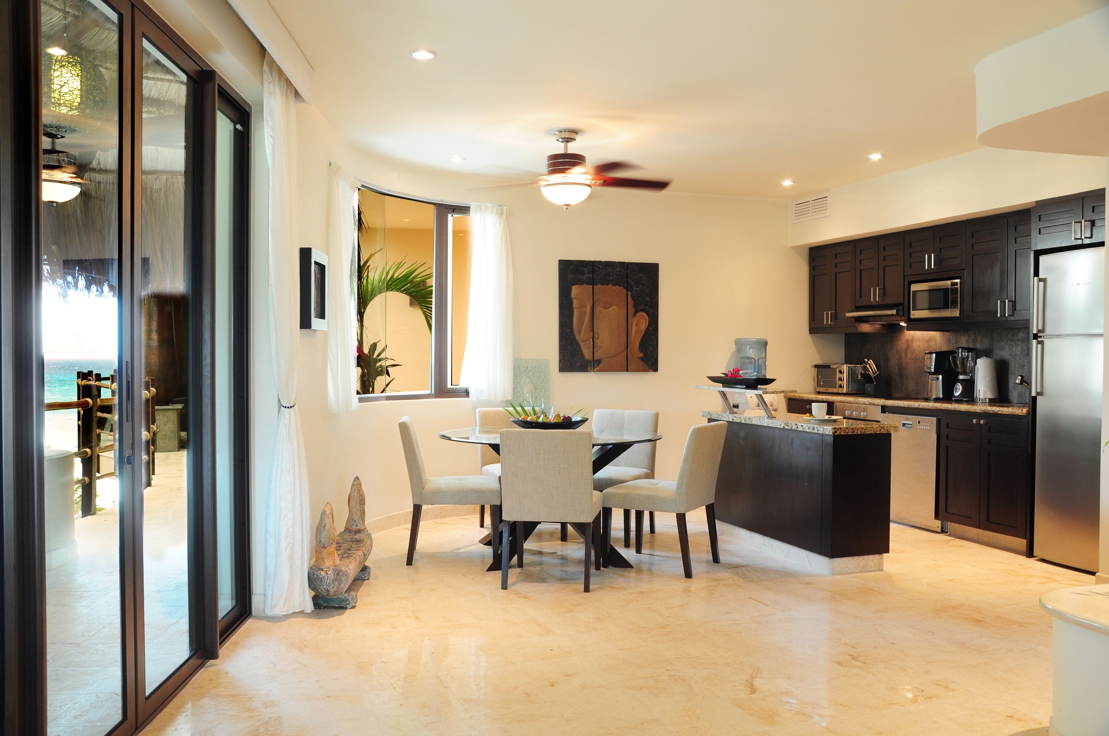 A modern kitchen with a dining area, featuring a large island, dark cabinetry, and a ceiling fan.