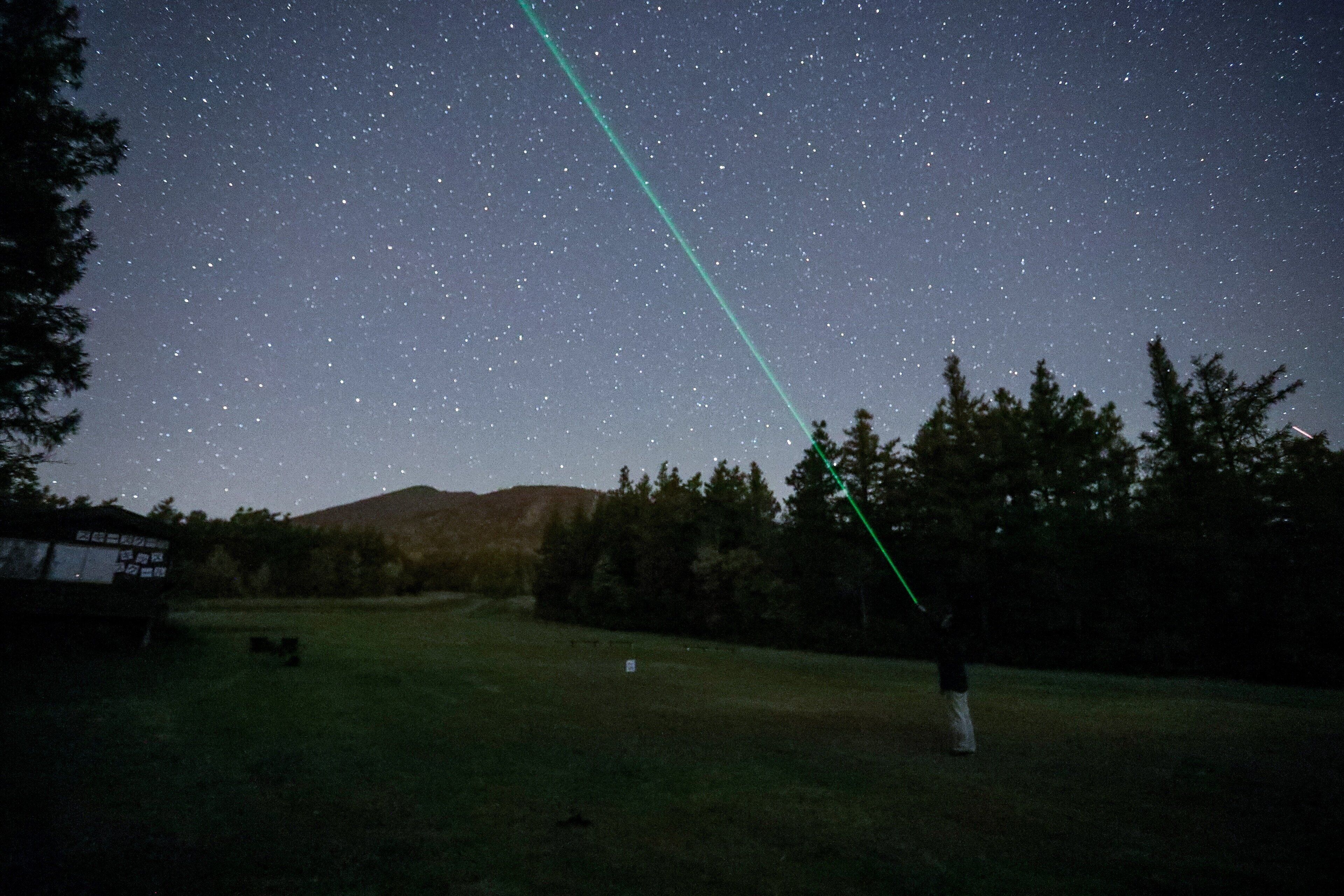 A starry night sky with a visible green laser beam.