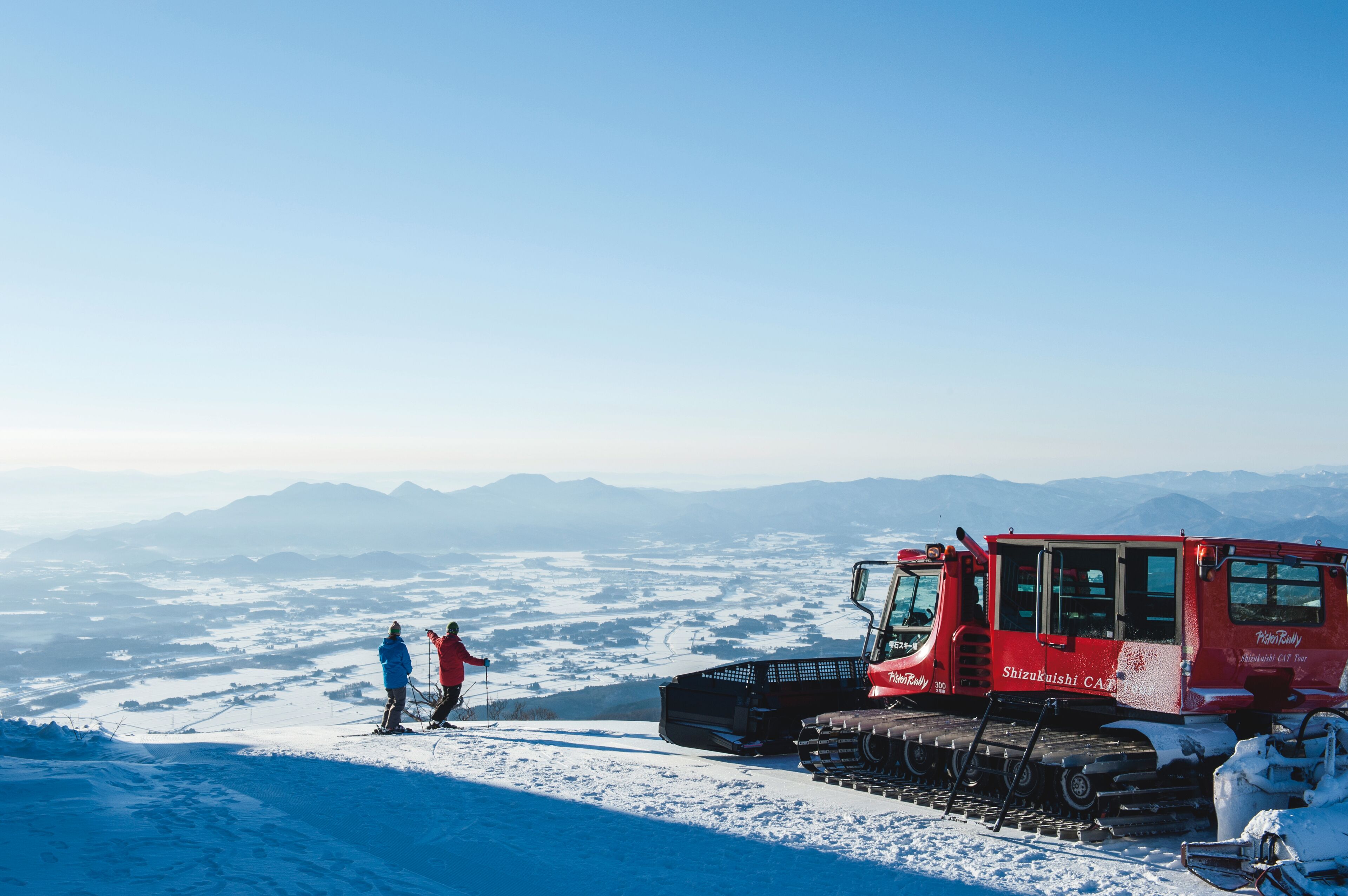 Paisaje nevado con una moto de nieve roja y dos personas con equipo de esquí.