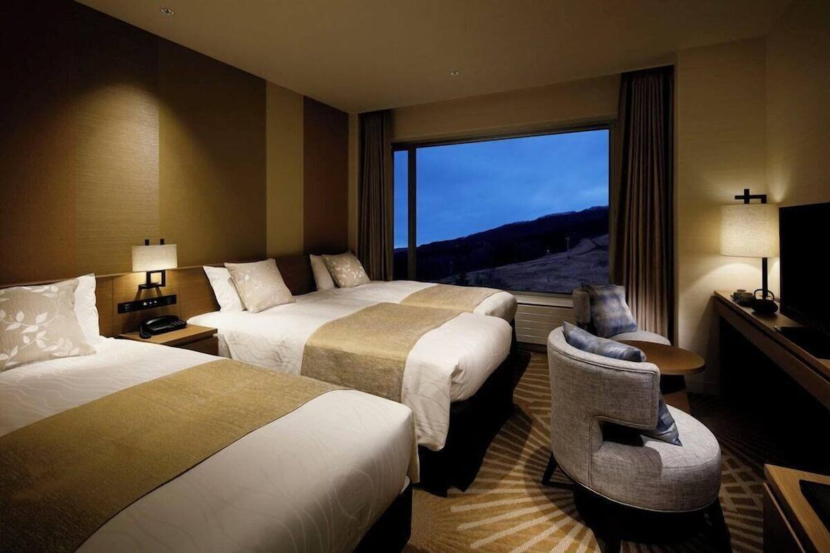 A hotel room with two beds, a sofa, a TV, and a large window with a view.